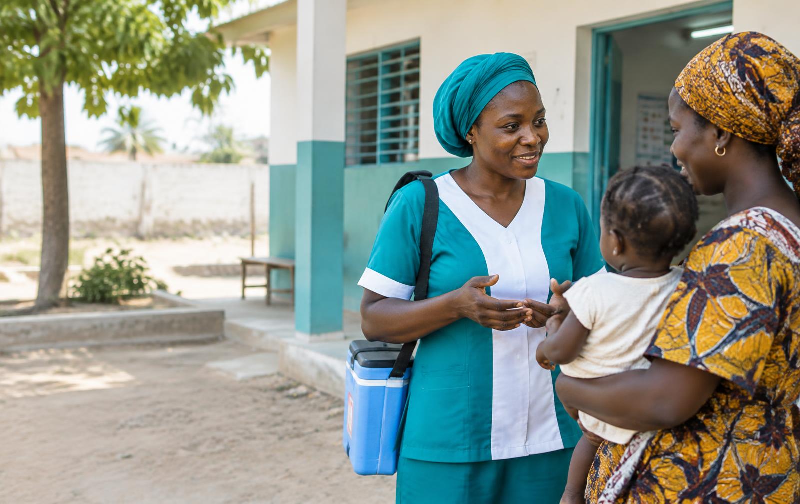 Une agente de santé échange avec une mère et son enfant devant un centre de santé